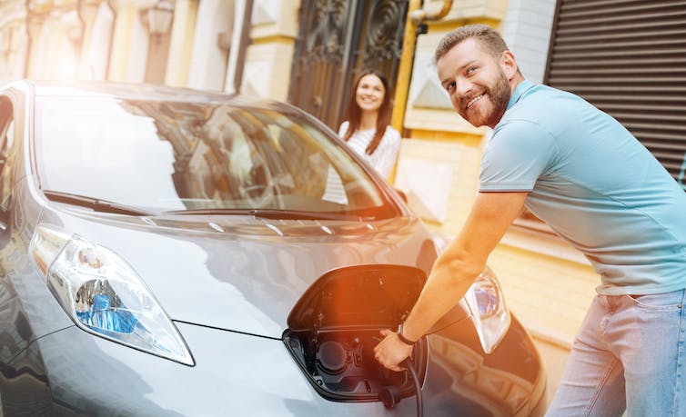 Smiling man plugs in electric car.